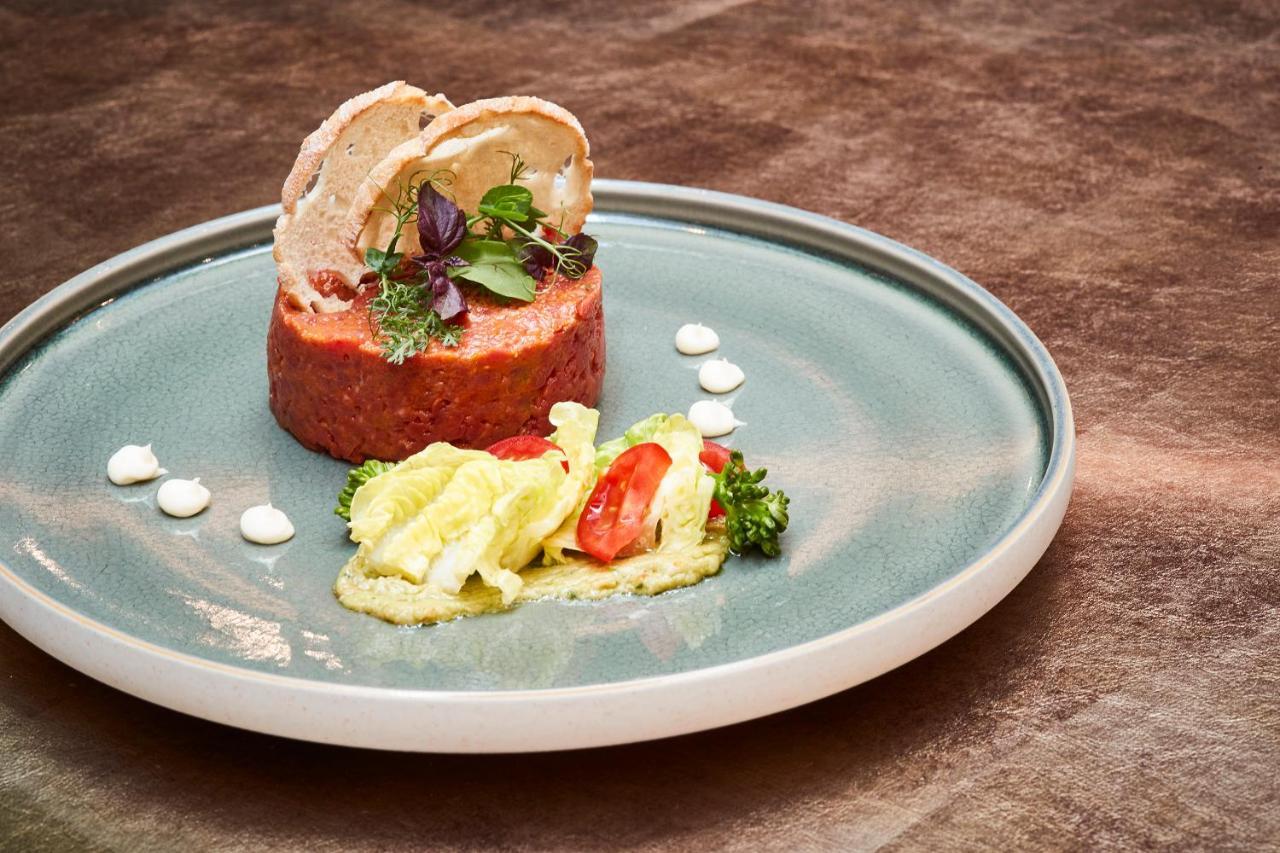 Steigenberger Hotel Herrenhof Vienna Esterno foto The photo showcases an elegantly plated dish. At the center, there is a round presentation of a textured paté or terrine, decorated with slices of meat on top and garnished with fresh herbs. Accompanying this are colorful elements on the plate, inclu